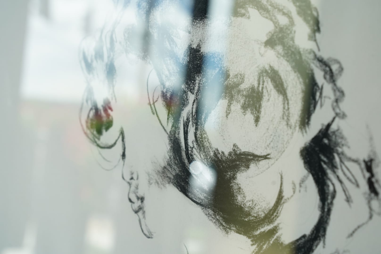 La Collezione Studio 32 Un disegno a matita dell'artista Alex Righetto, che raffigura un volto astratto con una miscela di linee sfumate e un tocco di colore, esposto su una superficie riflettente.